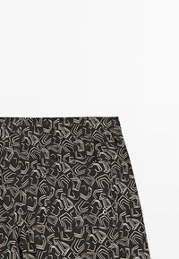 Černé šortky s bílými abstraktními geometrickými liniemi, vybavené elastickým pasem a kapsou s malým kovovým okem.