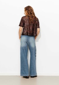Top en sequins marron à manches courtes associé à un jean en denim taille haute et large avec un délavage clair et un effet dégradé subtil.