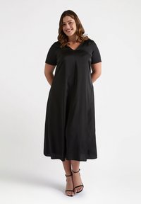 Vestido negro de manga corta con escote en V, con una silueta en A fluida y textura suave. Llevado con sandalias negras con tiras.