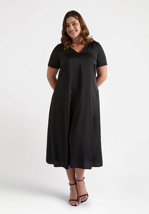 Black, short-sleeved dress with a V-neckline, flowing A-line silhouette, and smooth texture. Worn with black strappy sandals.