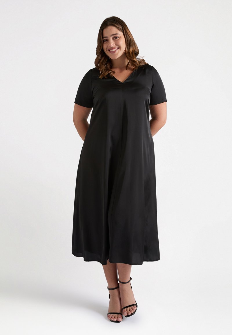 Vestido negro de manga corta con escote en V, con una silueta en A fluida y textura suave. Llevado con sandalias negras con tiras.