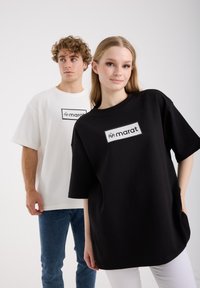 Zwart-witte oversized t-shirts gemaakt van zacht katoen, met een rechthoekig logo in het midden. Modellen poseren tegen een witte achtergrond.