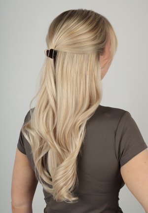 Femme blonde aux longs cheveux ondulés, mi-attachés avec une pince noire, portant un t-shirt gris foncé à manches courtes, vue de dos.