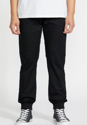 Zwarte jogger broek met een taperende pasvorm, elastische boorden en zijzakken, gecombineerd met zwarte high-top sneakers met witte veters.