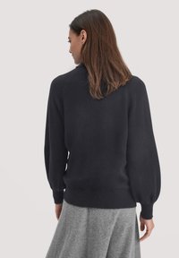 Schwarzer gestrickter Pullover mit hohem Kragen, taillierter Taille und Ballonärmeln, kombiniert mit einem grauen Rock, der eine weiche Textur zeigt.