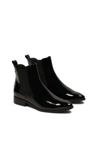 Botines de charol negro con punteras afiladas, paneles laterales elásticos y pequeñas lengüetas. Suelas de goma planas con una textura suave.