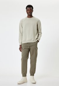 Lichtgrijze sweatshirt met raglanmouwen, gecombineerd met olijfgroene cargobroeken met zijzakken, en crèmekleurige hoge sneakers.