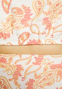 Tecido estampado com desenhos de paisley em rosa e laranja sobre um fundo claro, com detalhes franzidos ao longo da borda superior.