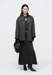 Tamsiai pilkas vilnonis paltas su apykakle, derinamas su atitinkamu megztiniu ir sijonu. Priedai apima juodus odinius pirštines ir maišelį. Juodi aulinukai su kulnais.