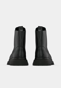 Μαύρες δερμάτινες μπότες μέχρι τον αστράγαλο με ομαλή υφή, ανθεκτικές καουτσούκ σόλες, χερούλια στο πίσω μέρος και ραφές γύρω από τις ραφές.