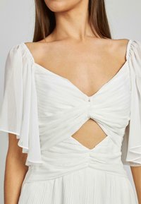 Weißes Kleid mit Herzausschnitt, plissierter Textur und kurzen durchsichtigen Ärmeln. Verfügt über ein zentrales Drehdetail und einen Ausschnitt an der Taille.