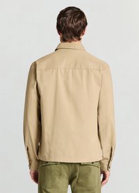 Beige Baumwolljacke mit spitzem Kragen, langen Ärmeln und geknöpften Manschetten. Der Rücken hat einen geraden Schnitt und minimale Nähdetails.
