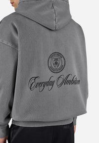 Grijze sweatshirt met capuchon, voorzien van een groot rond logo en de tekst "Everyday Ambition" op de achterkant in zwart, geribbelde mouwen en onderrand.