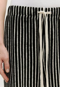 Tissu rayé noir et blanc avec une finition texturée, doté d'une taille à cordon de serrage et de détails de couture apparents.