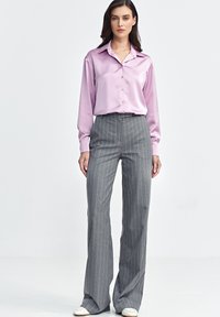 Różowa satynowa koszula zapinana na guziki z kołnierzykiem, w połączeniu z szarymi spodniami w prążki o rozszerzanym kroju. Spodnie mają wysoki stan i szeroką nogawkę.