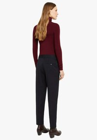 Dolcevita color bordeaux abbinato a pantaloni sartoriali blu navy. Presenta un collo alto, una vestibilità aderente e un dettaglio con bottoni neri sul retro dei pantaloni.