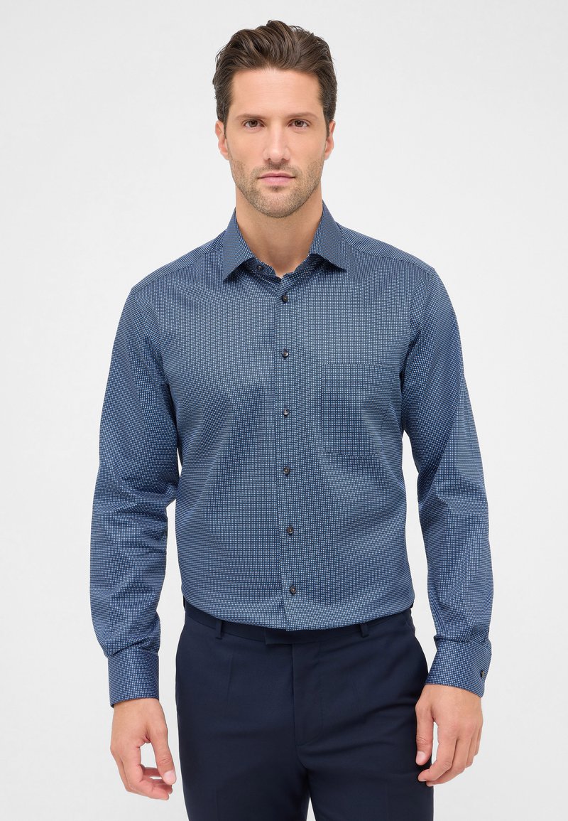 Camicia azzurra con bottoni, caratterizzata da un piccolo motivo geometrico, maniche lunghe e taschino sul petto. Il tessuto è liscio e la vestibilità è aderente.