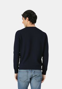 Maglione blu navy con collo rotondo e maniche lunghe, caratterizzato da orlo e polsini a coste. Indossato con jeans azzurri, mostrando una consistenza liscia.