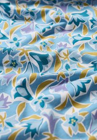 Ziedu raksta audums gaiši zils, ar zaļām, purpura un tumši z blue ziediem, gluda tekstūra un maigs kritums.