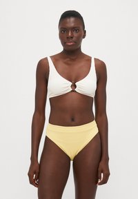 Haut de bikini texturé blanc avec un détail en métal à l'avant, associé à un bas de bikini jaune taille haute. Tissu lisse, design minimaliste.