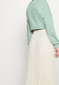 Maglione cropped verde menta con spalle scese abbinato a una gonna crema plissettata in vita alta con un tessuto testurizzato.