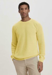 Gelbes Strickpullover mit strukturiertem Rippmuster, Rundhalsausschnitt und langen Ärmeln. Der Stoff wirkt leicht und atmungsaktiv.