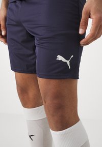 Jūrų pajėgų treniruočių šortai, pagaminti iš lygaus audinio, su balta Puma logo ant šlaunies. Derinami su baltais kojiniais, kurių tekstūra yra rafinuota.