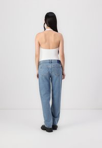 Un body blanc à col halter avec un dos ouvert, associé à un jean taille haute bleu clair, doté de poches arrière, d'une coupe droite et d'un ourlet brut.