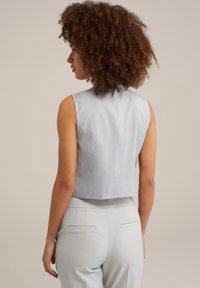 Top corto senza maniche in tessuto grigio chiaro, caratterizzato da una texture liscia e linee pulite. Indossato con pantaloni coordinati grigio chiaro, mostrato da dietro.