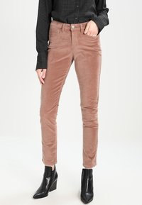 Kordové kalhoty v tlumené růžové barvě, s úzkým střihem, jemnou texturou, předními kapsami a knoflíkovým zapínáním, doplněné černými kotníkovými botami.