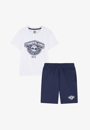 Maglietta bianca Timberland a maniche corte con stampa del logo abbinata a pantaloncini blu navy con vita elastica e un piccolo logo abbinato sulla gamba.