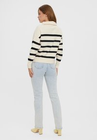 Knit sweater in cream with black horizontal stripes, featuring a fold-over collar. Paired with light blue jeans and yellow block-heel shoes.