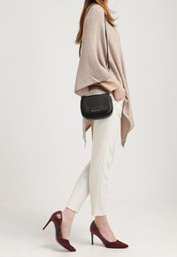 Beige poncho-tröja, krämfärgade tajta byxor, vinröda klackar och svart axelväska med guldfärgade detaljer. Enkel design, mjuka texturer.