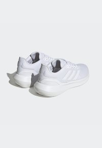 Scarpe sportive bianche con tomaia in rete per traspirabilità, suola in gomma liscia e tre distinti dettagli a strisce sui lati.