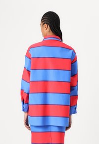 Pitkähihaisessa paidassa on punaiset ja siniset raidat, rento malli, kaulukset ja nappi- sekä hihansuut. Kankaan pinta on sileä ja helma on huolellisesti viimeistelty.