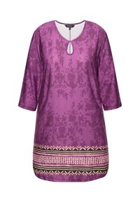 Lila Tunika mit 3/4-Ärmeln, mit einem Schlüsselloch-Ausschnitt und dekorativem Saum mit schwarzen, beigen und weißen geometrischen Mustern.