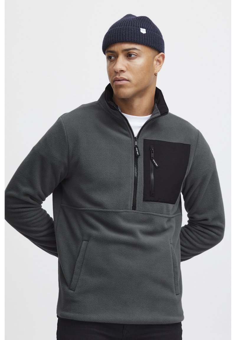 Pullover in felpa grigia con una tasca sul petto nera con zip, colletto a mezza zip e tasche laterali. Texture morbida, taglio dritto e polsini a coste.