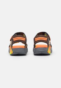 Svarte og oransje åpne sandaler med justerbare stropper, teksturerte såler og neongrønne detaljer, som har et robust design for komfort.