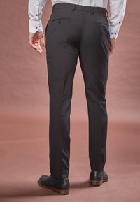 Pantaloni negri eleganți, cu o textură netedă, ajustați pe corp și cu buzunare la spate. Purtați cu o cămașă de culoare deschisă și pantofi negri de dress.
