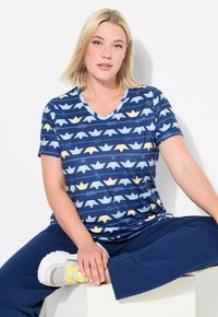 Námořnické tričko s V výstřihem a potiskem papírových lodí v modré a žluté barvě. Doplněné námořnickými kalhotami a světle šedými teniskami.