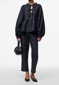 Ensemble texturé bleu marine composé d'un haut ample avec une ouverture en forme de goutte d'eau, un détail noué, et un pantalon assorti à coupe slim. Accompagné d'un sac à main noir.