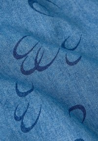 Blå denimtyg med en subtil textur, med mörkblå abstrakta mönster över ytan som skapar en lagrad visuell effekt.