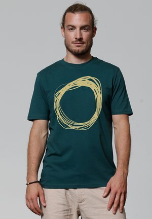 Teal katoenen t-shirt met een cirkelvormig geel grafisch ontwerp, korte mouwen, ronde hals en een relaxte pasvorm.