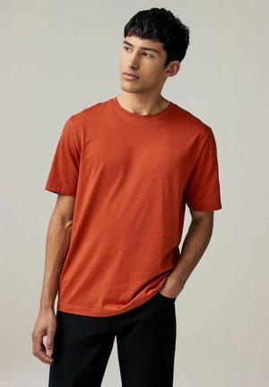 Kortærmet T-shirt med rund hals i brændt orange bomuldsstof, parret med sorte bukser, med en afslappet pasform og glat tekstur.