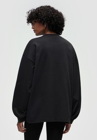 Sweatshirt nero oversize con maniche lunghe e voluminose, scollatura a girocollo e texture liscia. Presenta una vestibilità morbida e spacchi laterali.