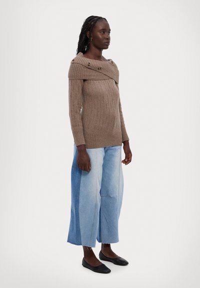 Pull en tricot côtelé marron avec un design épaule dénudée et des accents de boutons, associé à un pantalon en denim bleu clair à jambes larges avec un effet de color-block.