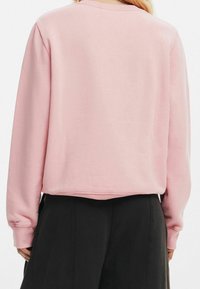 Rosa bomullströja med långa ärmar, rund halsringning och en avslappnad passform. Mjuk textur och fåll som är något kortad vid midjan.