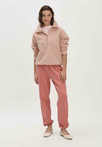 Helles rosa Fleece-Halbzip-Pullover mit langen Ärmeln und Stehkragen, kombiniert mit passenden rosa Jogginghosen mit elastischen Bündchen.