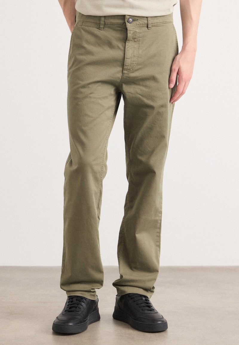 Olive green cotton pants with a straight-leg design, zip fly, and button closure. Worn with black sneakers, featuring a smooth texture.