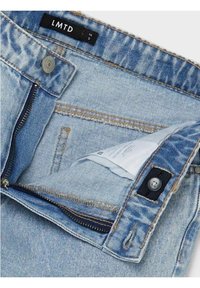 Ljusblå denimjeans med dragkedja och knappstängning, som har en dold ficka inuti midjebandet och en etikett med texten "LMTD."